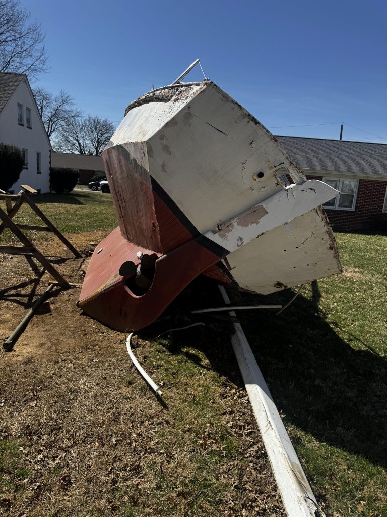 Abandoned boat discarded in a landfill, surrounded by piles of trash and debris.